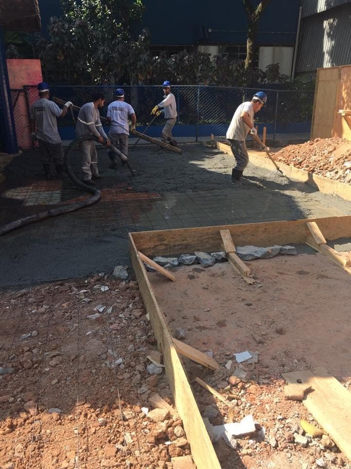 Equipe espalhando concreto sobre a armação do piso do pátio, com fôrmas de madeira.