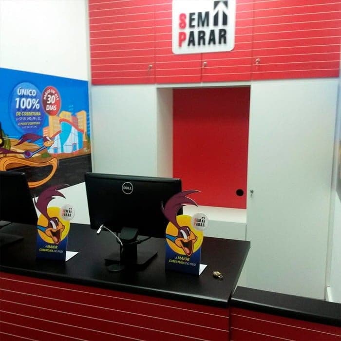 Balcão de atendimento vermelho da loja Sem Parar, com painel da marca na parede.