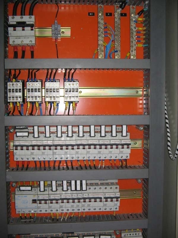 Quadro de distribuição elétrica aberto, com disjuntores montados sobre placa laranja.
